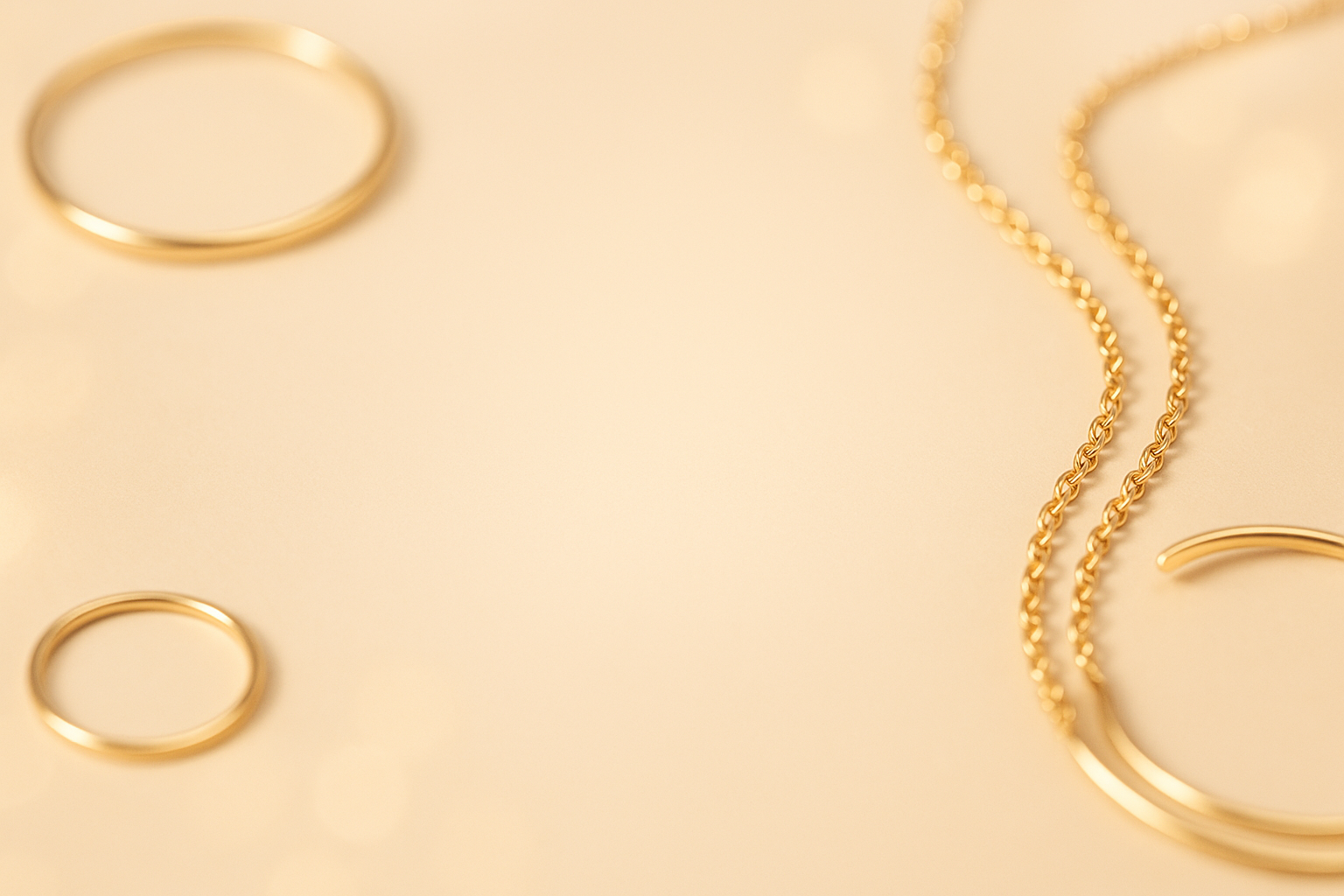 A luxurious jewelry banner background for an elegant online store. Minimalistic but premium style. Soft beige and warm golden tones, with subtle reflections of gold jewelry (rings, bracelets, necklaces) arranged in the background in a blurred, aesthetic way. Leave a clean central area with smooth gradient for overlay text. The design should feel modern, high-end, and feminine, with lots of light and clarity to ensure the text remains easy to read.”